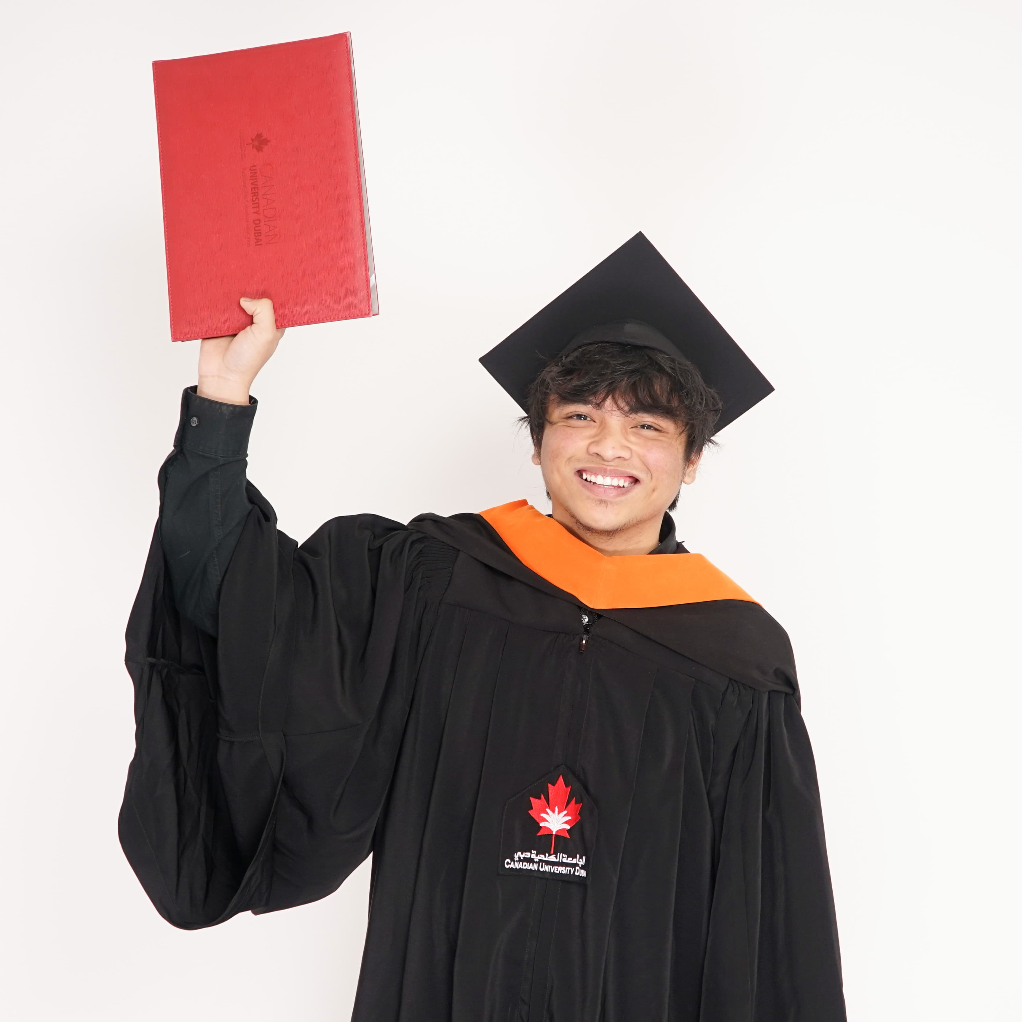 Cap tilted back, holding up the red Canadian University Dubai diploma folder